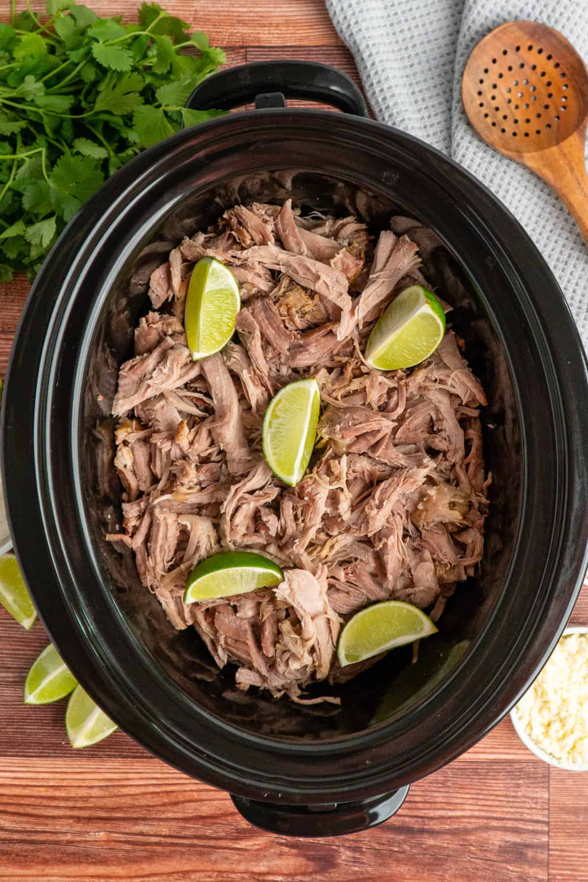 Pork carnitas in a slow cooker garnished with limes.