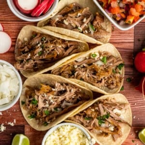 Five pork carnitas tacos garnished with cilantro, onions and cheese.
