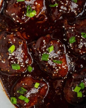 Honey garlic chicken in a crock pot garnished with sesame seeds and green onions.