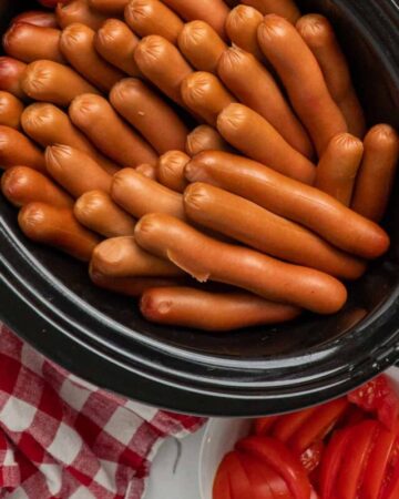 Cooked hot dogs in a black oval crock pot.