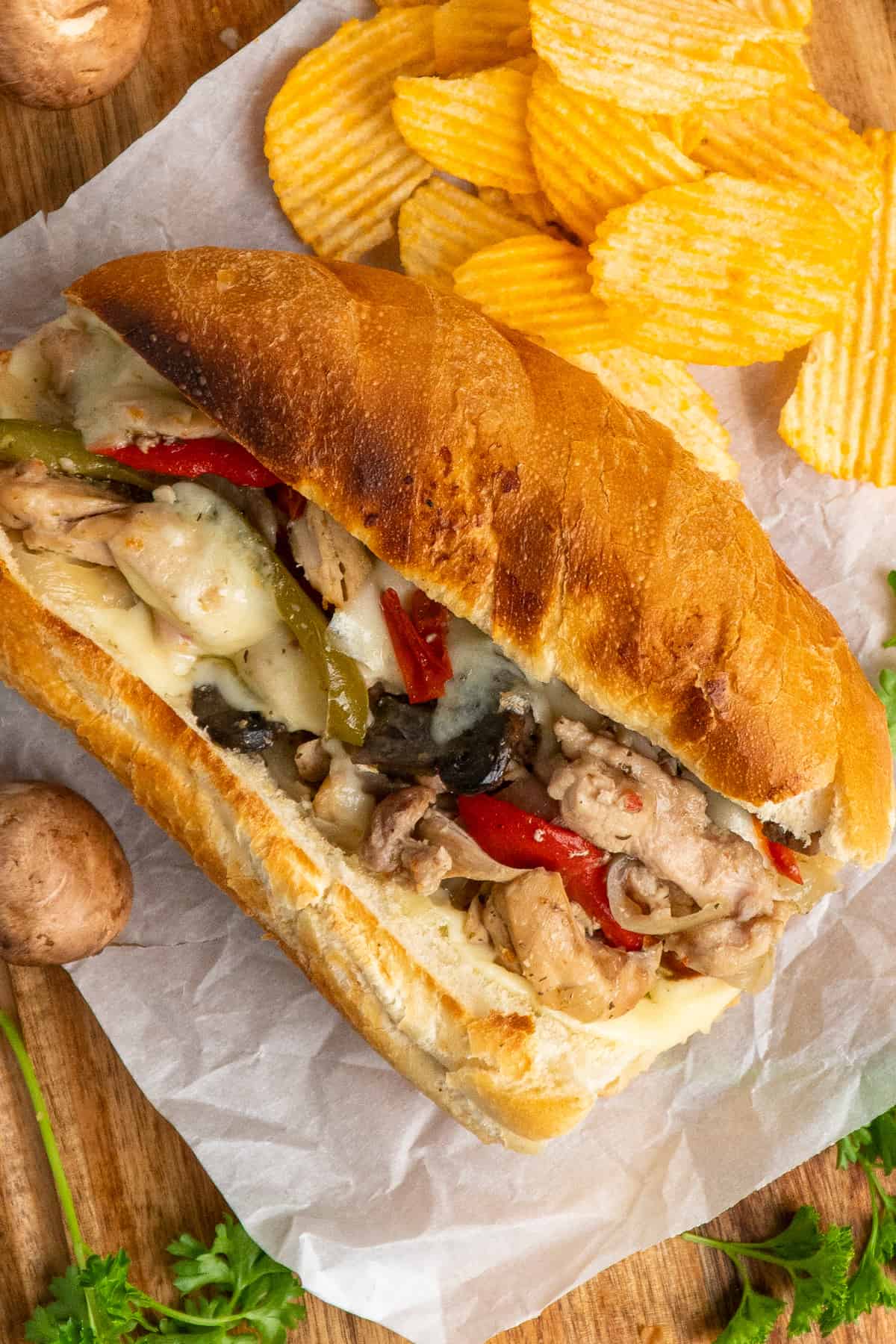 Close-up of chicken philly cheesesteak on a toasted bun with chips in the background.