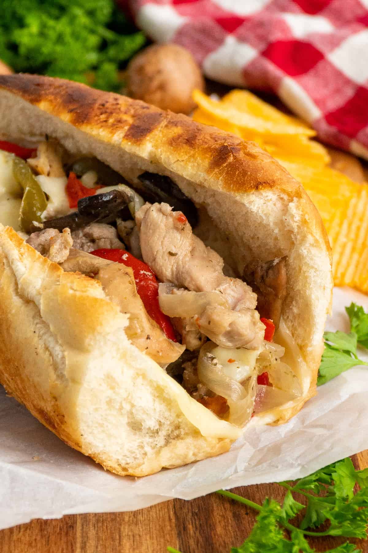 Close-up of chicken philly cheesesteak on a toasted bun with chips in the background.