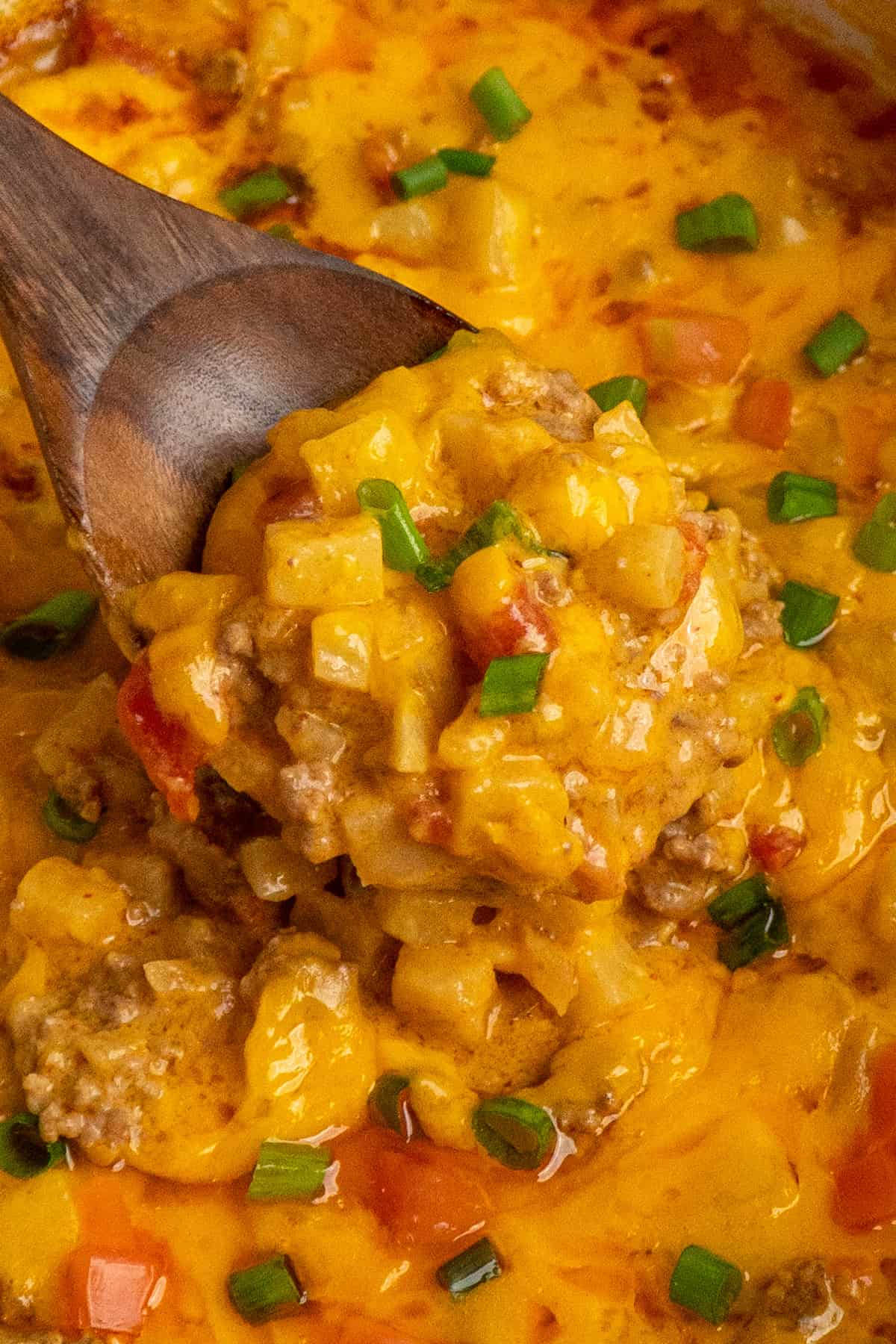 Close-up of crock pot beef potato taco casserole with a wooden spoon in it.