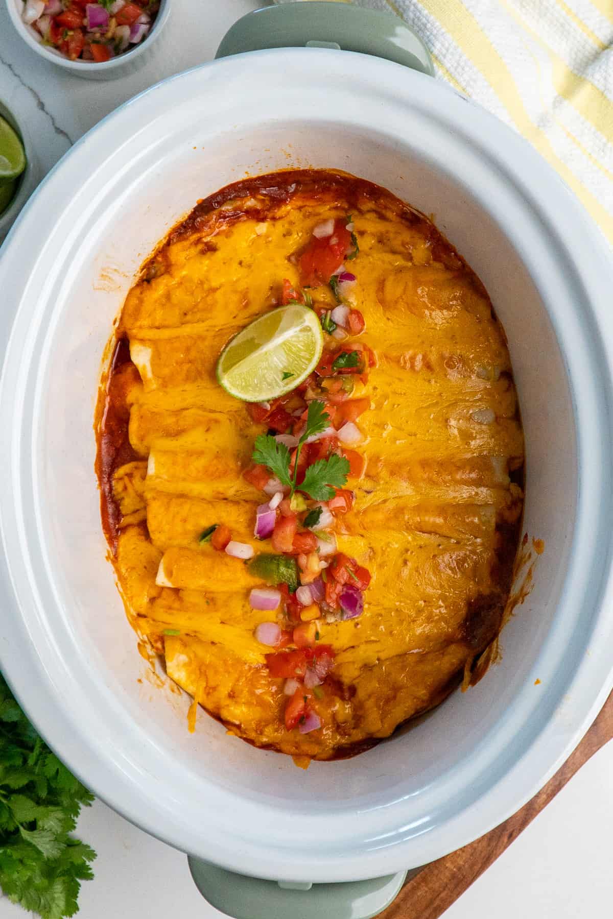 Crock Pot chicken enchiladas topped with pico de gallo and limes.