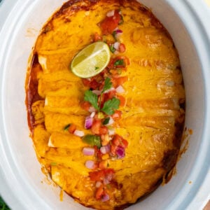 Crock Pot chicken enchiladas topped with pico de gallo and limes.