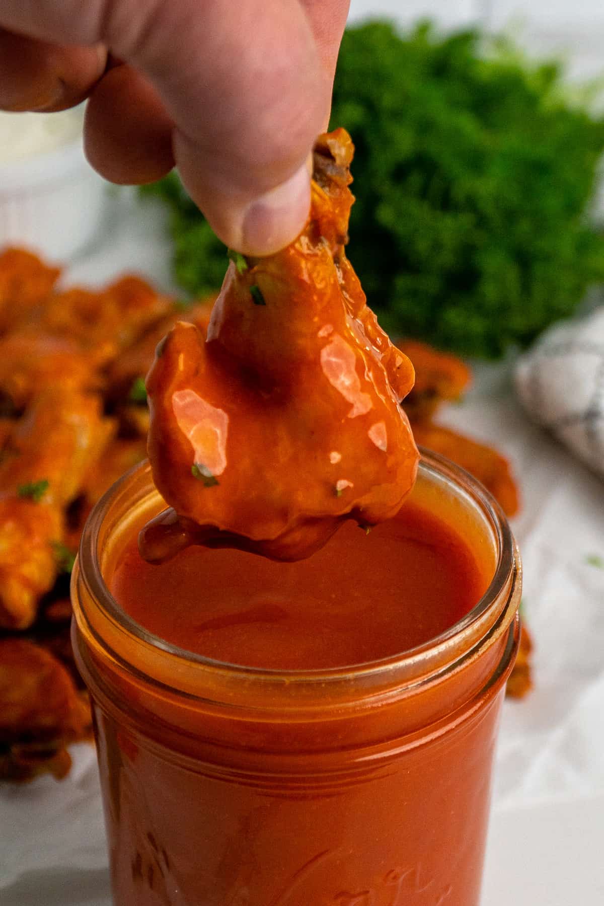A chicken wing being dipped into buffalo sauce.