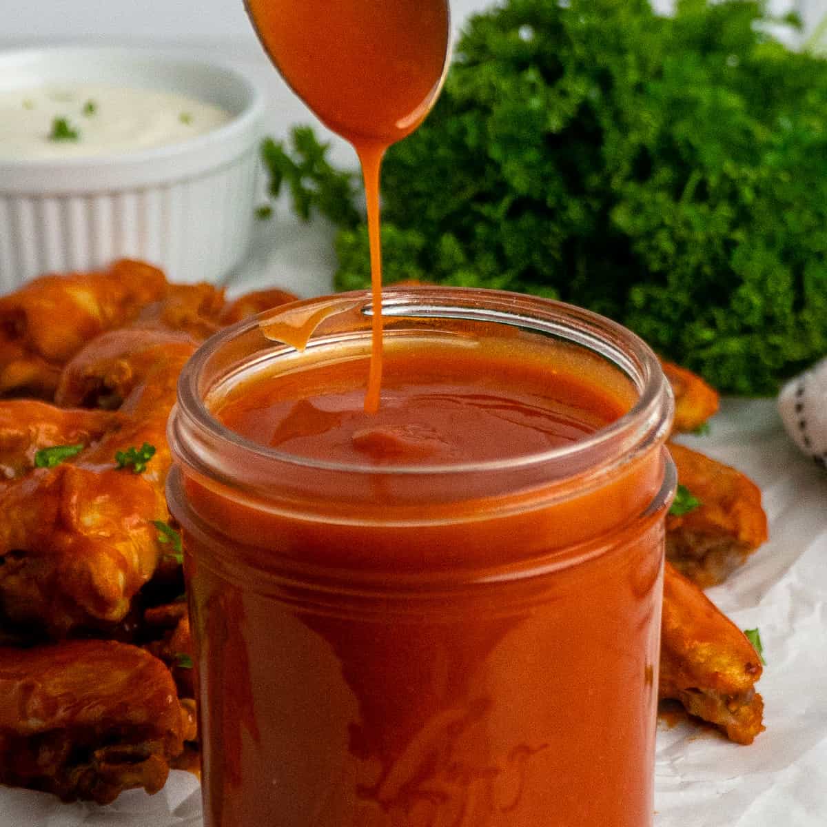 A spoon being dipped into homemade buffalo sauce.