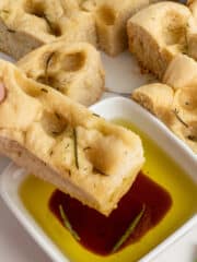 A hand dipping foccacia bread in olive oil and balsamic vinegar.