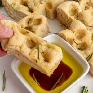 A hand dipping foccacia bread in olive oil and balsamic vinegar.