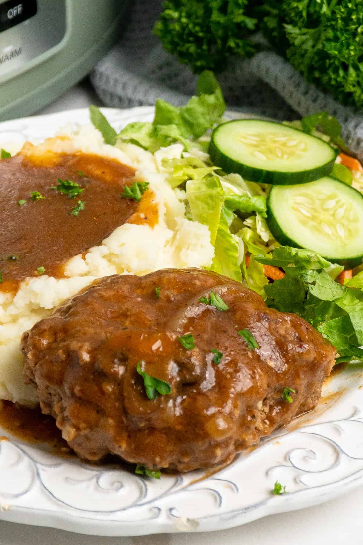 Close up of salsibury steak on a plate with mashed potatoes and salad.