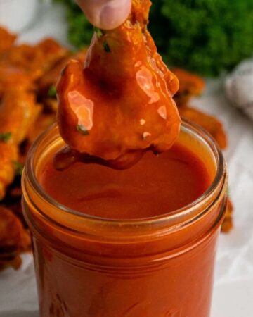 A chicken wing being dipped into buffalo sauce.