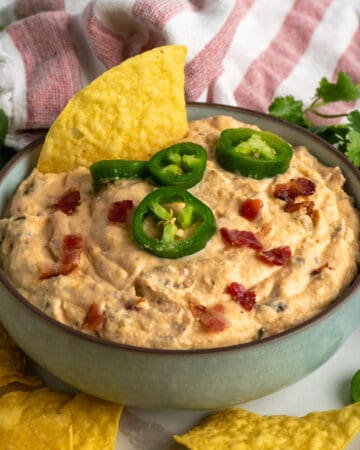 Close-up of Jalepeno popper dip in a bowl garnished with bacon and jalapenos.