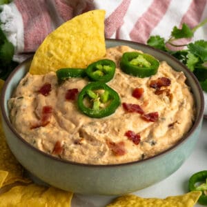 Close-up of Jalepeno popper dip in a bowl garnished with bacon and jalapenos.
