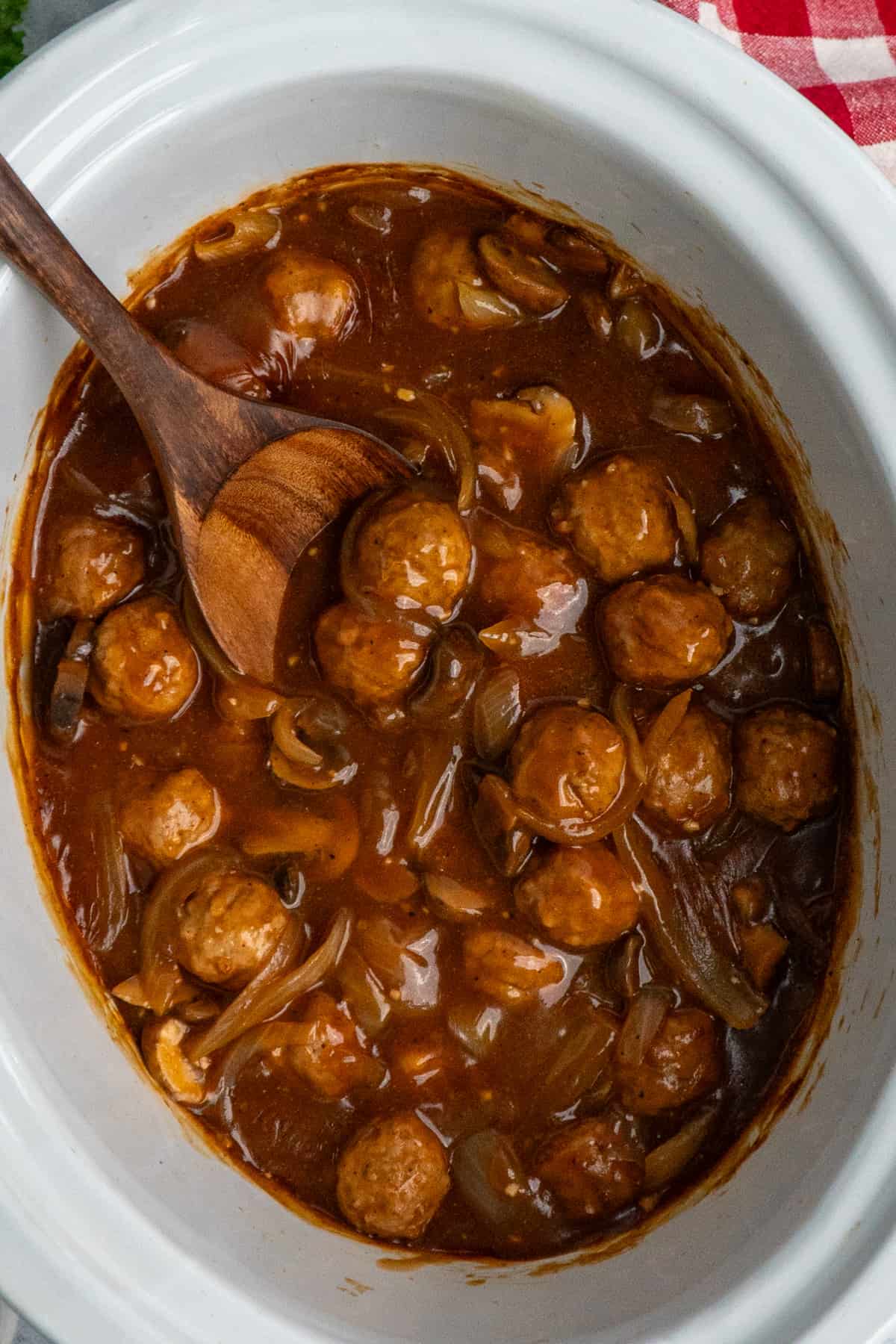 Salisbury steak meatballs in a crock pot with a wooden spoon.