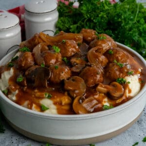 Overhead look at crock pot salisbury steak meatballs over a bowl of mashed potatoes.