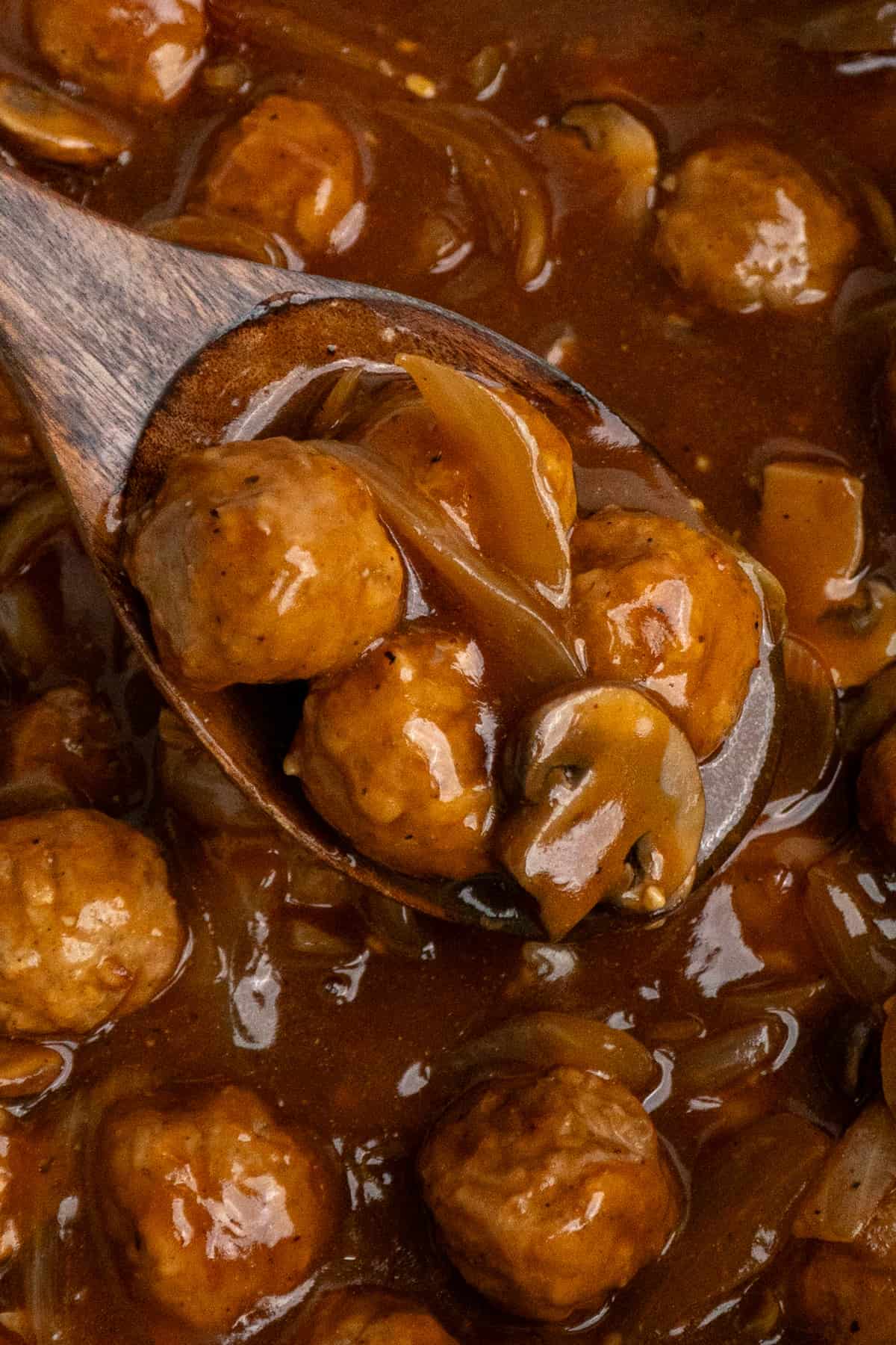 A wooden spoon holding salisbury steak meatballs ready to be served.