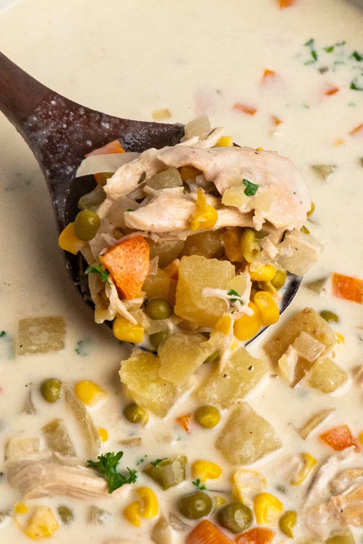 A wooden spoon scooping chicken pot pie soup.