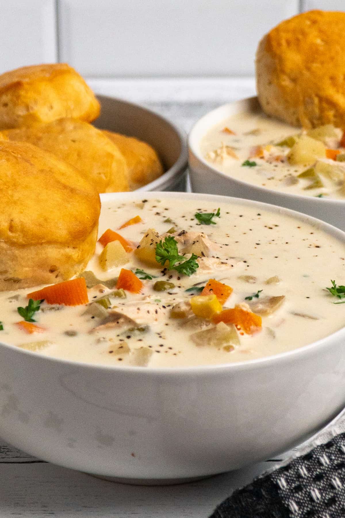Side view of chicken pot pie soup in a white bowl with a biscuit.