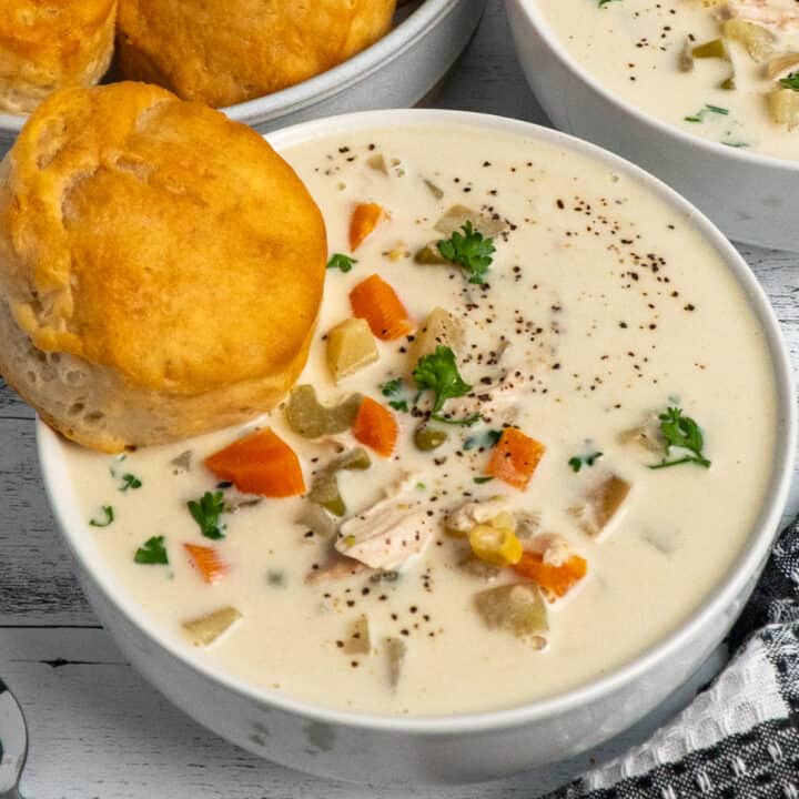 Crock pot chicken pot pie soup in a white bowl with a biscuit in it.