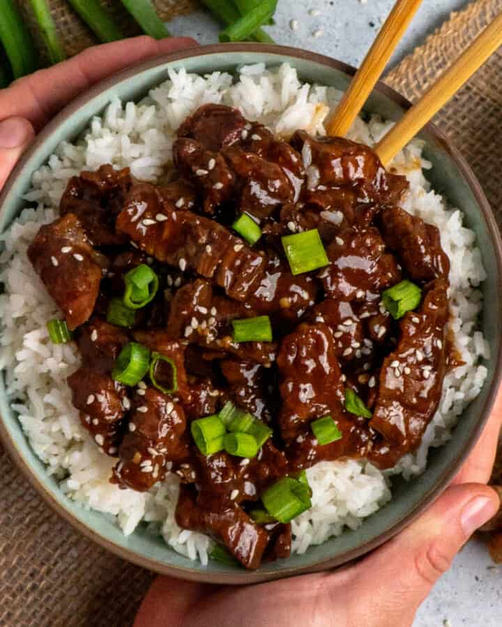 Hands holding a bowl of crock pot Korean beef over rice.