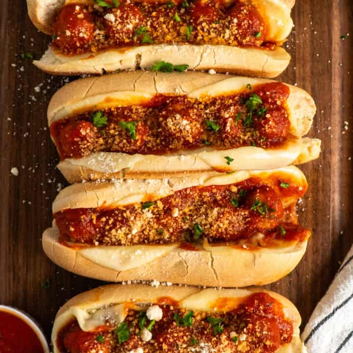 Overhead look of four crock pot meatball subs on a wood cutting board.