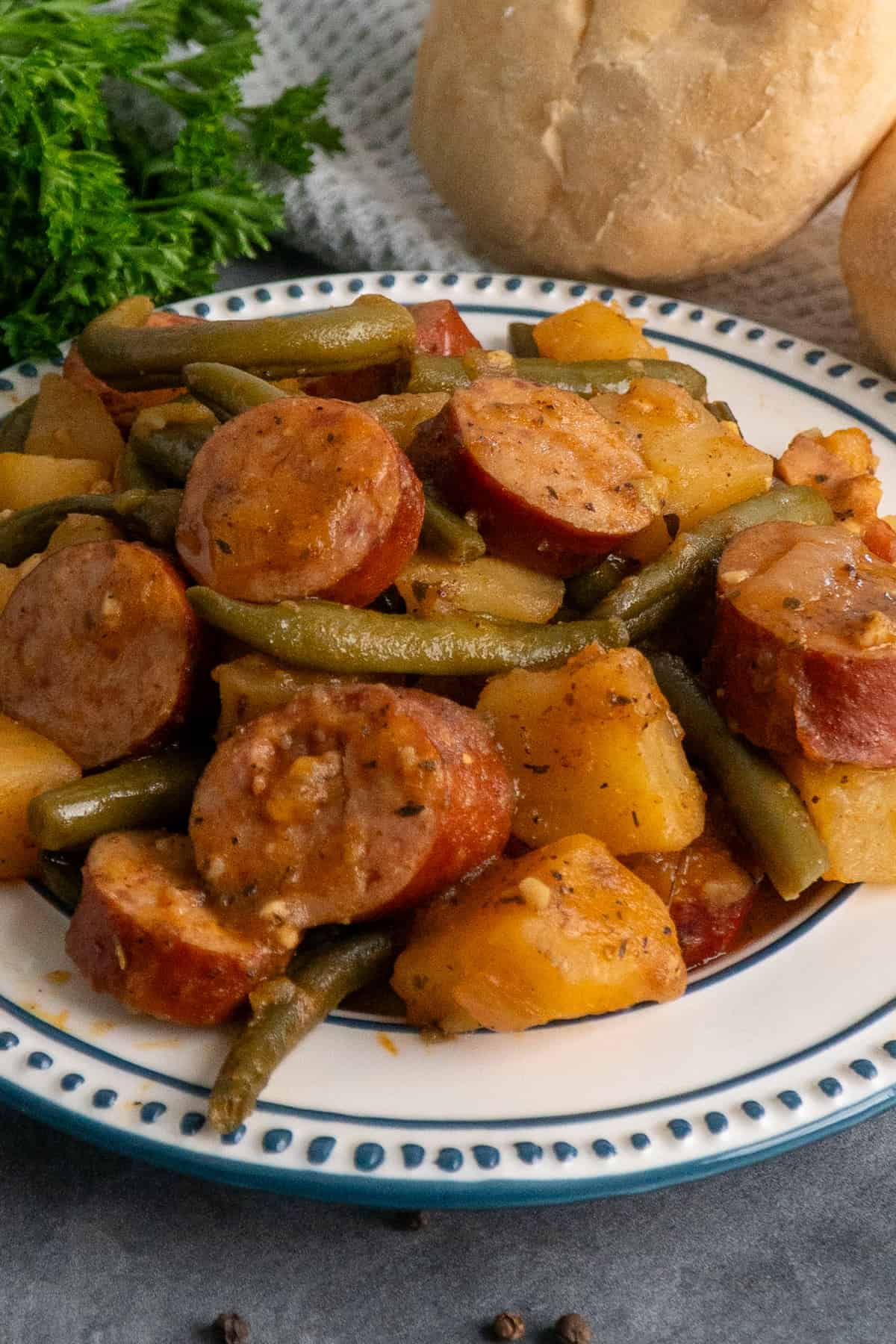 Close-up of crock pot sausage potatoes and green beans on a white plate.