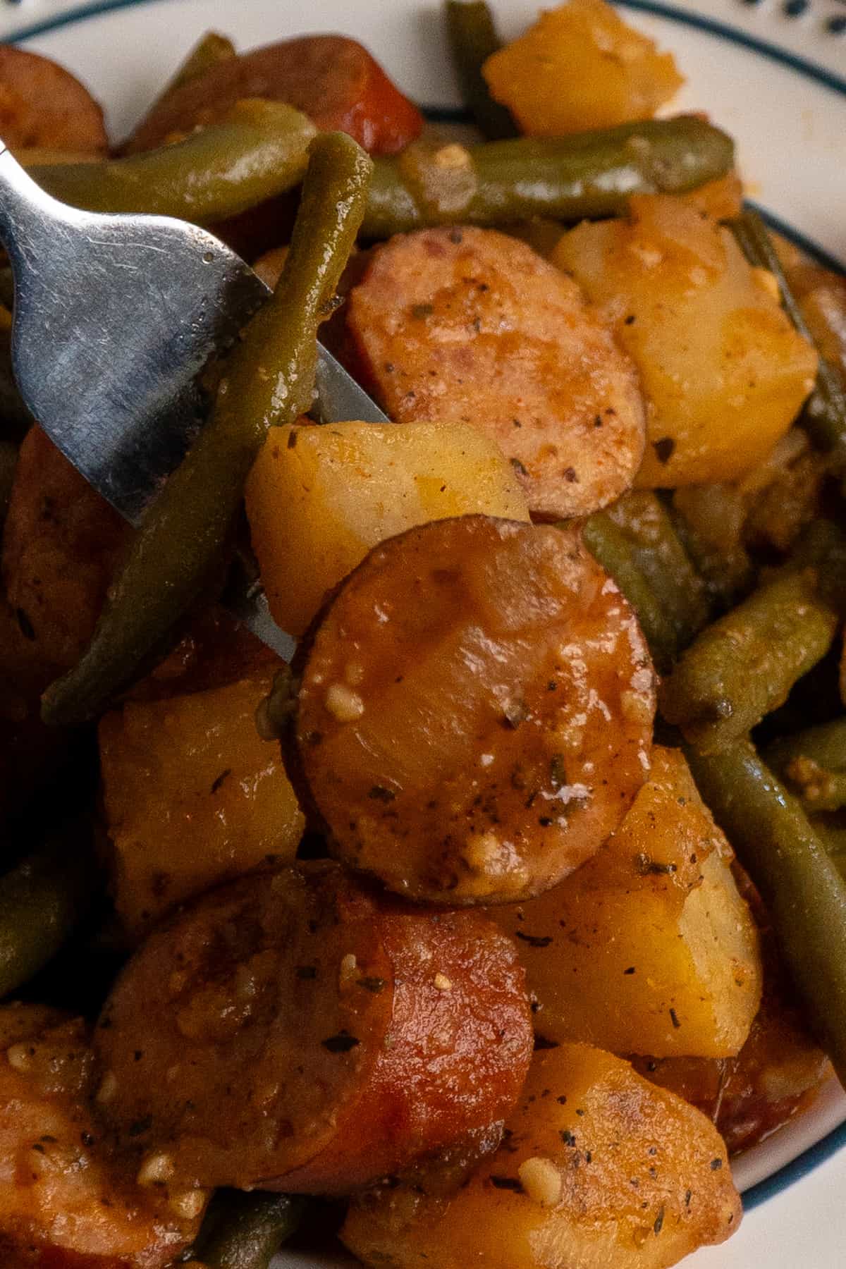 A fork holding a bite of sausage potatoes and green beans.