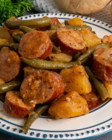 Close-up of crock pot sausage potatoes and green beans on a white plate.