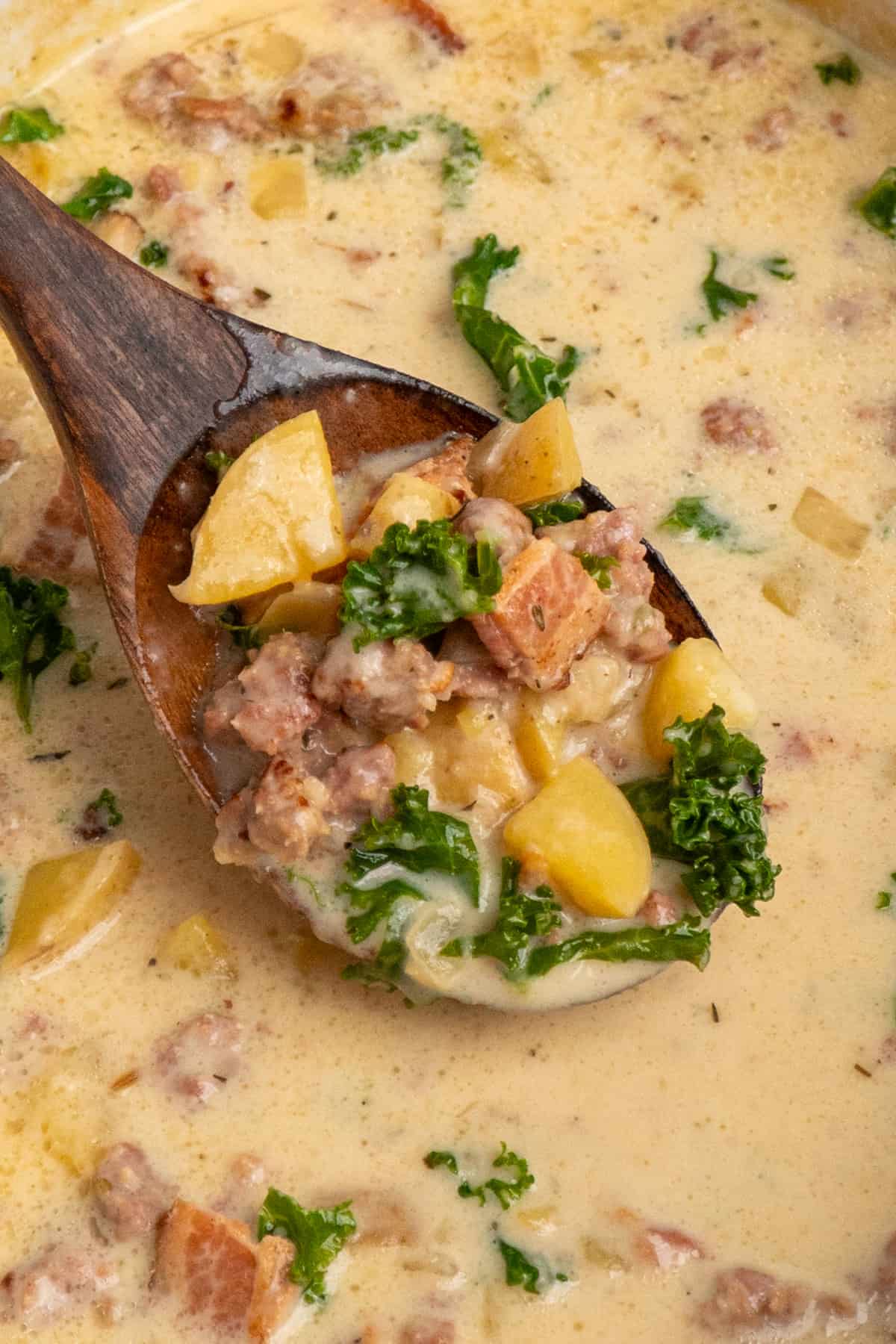 A wooden spoon holding a scoop of zuppa toscano soup.