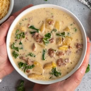 Hands holding a bowl of crock pot zuppa toscano soup.