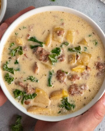 Hands holding a bowl of crock pot zuppa toscano soup.