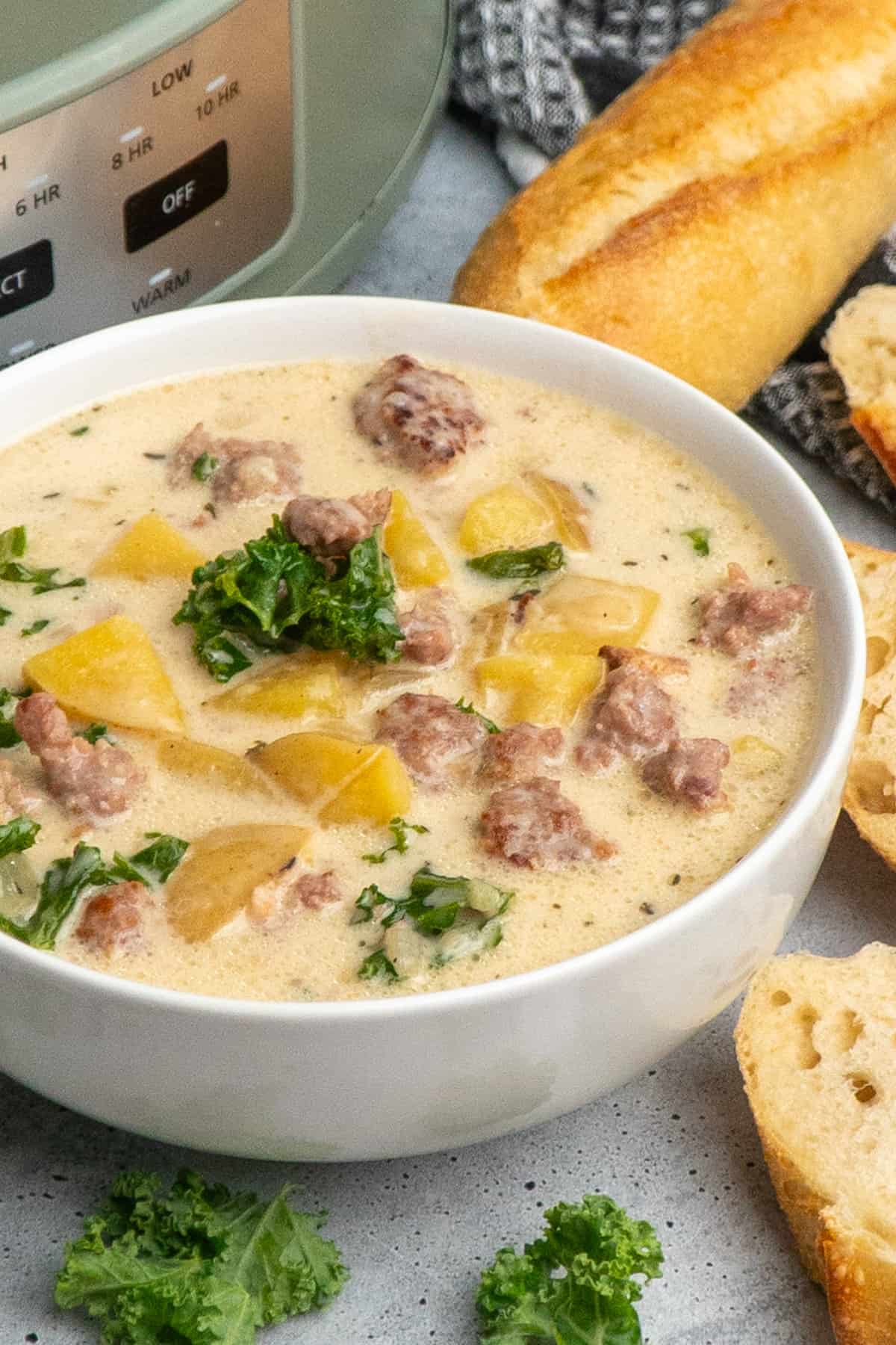 Close-up of zuppa toscano soup in a white bowl with bread in the background.