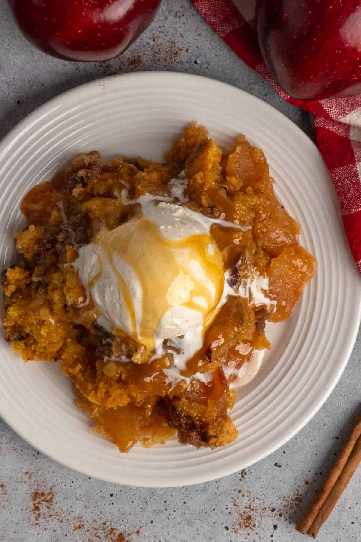 Overhead, look at apple cobbler on a plate with ice cream and caramel sauce.