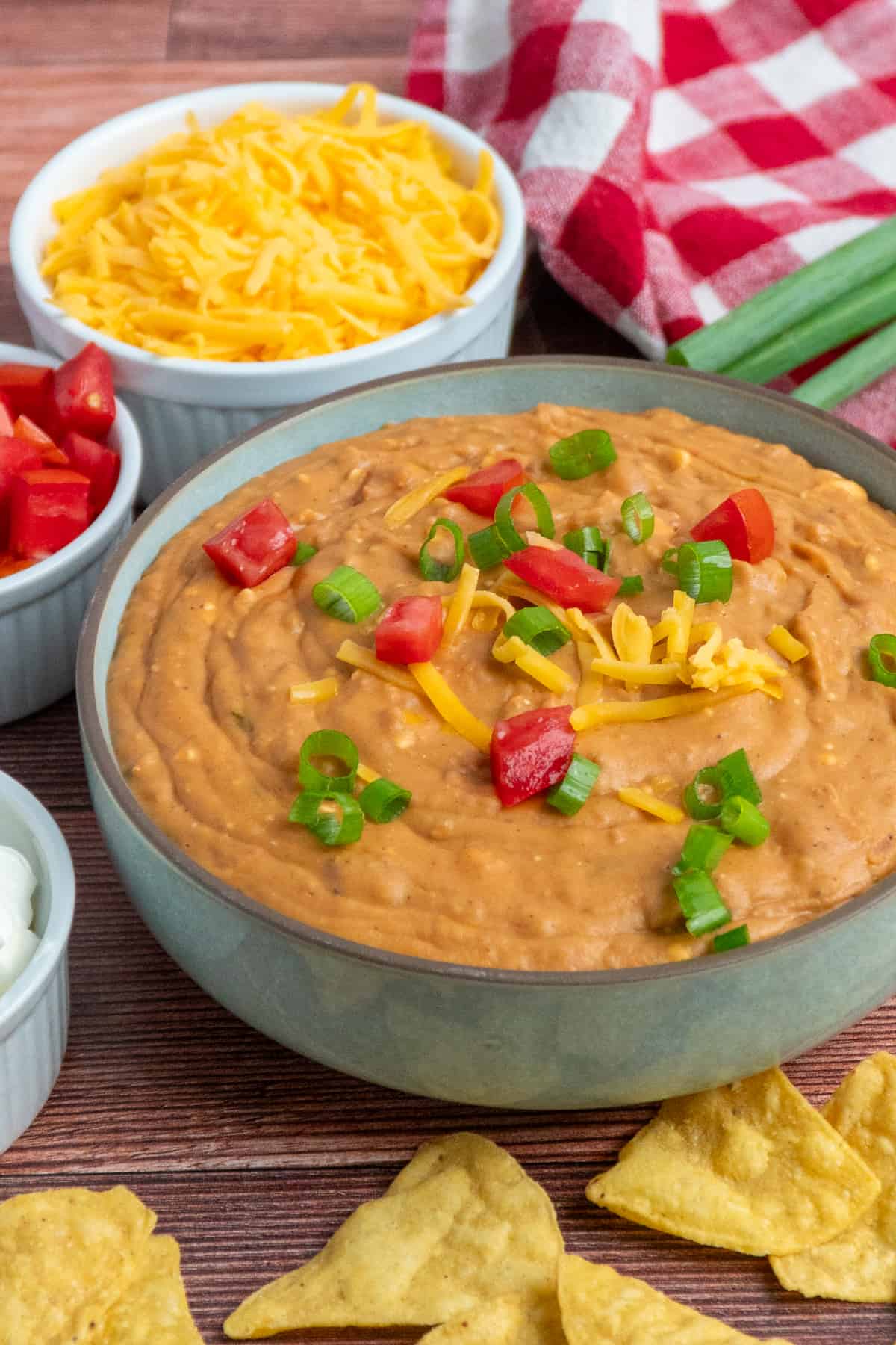 Close up of bean dip in a bowl with toppings in the background.