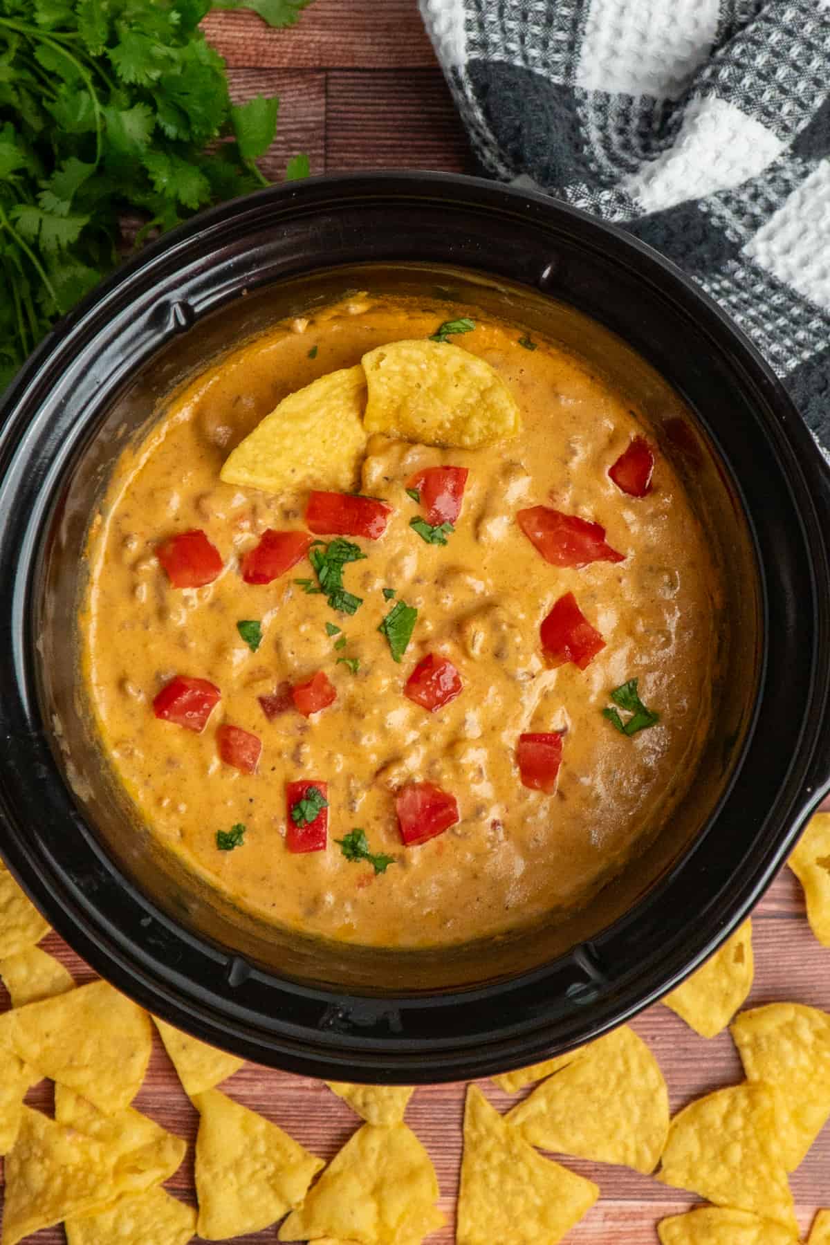 Overhead, look at crock pot cheeseburger dip garnished with tomatoes and cilantro.