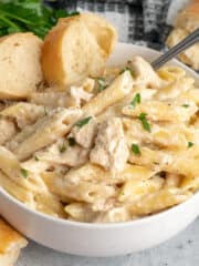 Crock pot chicken alfredo in a white bowl with pieces of bread.