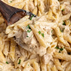 A wooden spoon holding a scoop of crock pot chicken alfredo over a slow cooker.