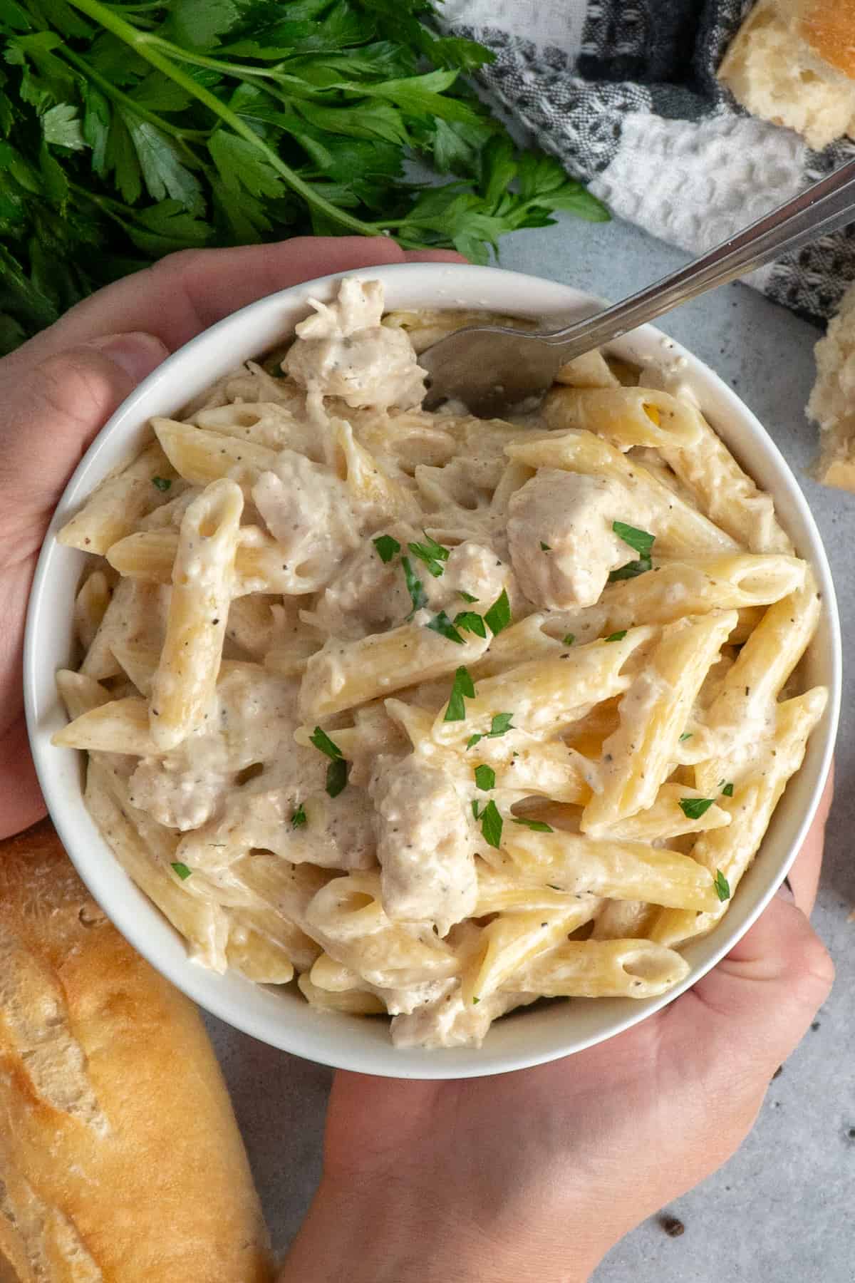 Hands holding a bowl of chicken alfredo.