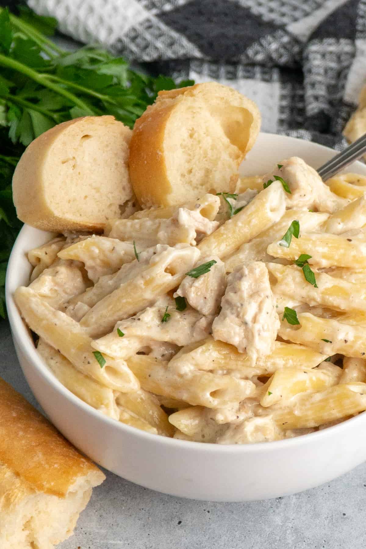 Crock pot chicken alfredo in a white bowl with pieces of bread.