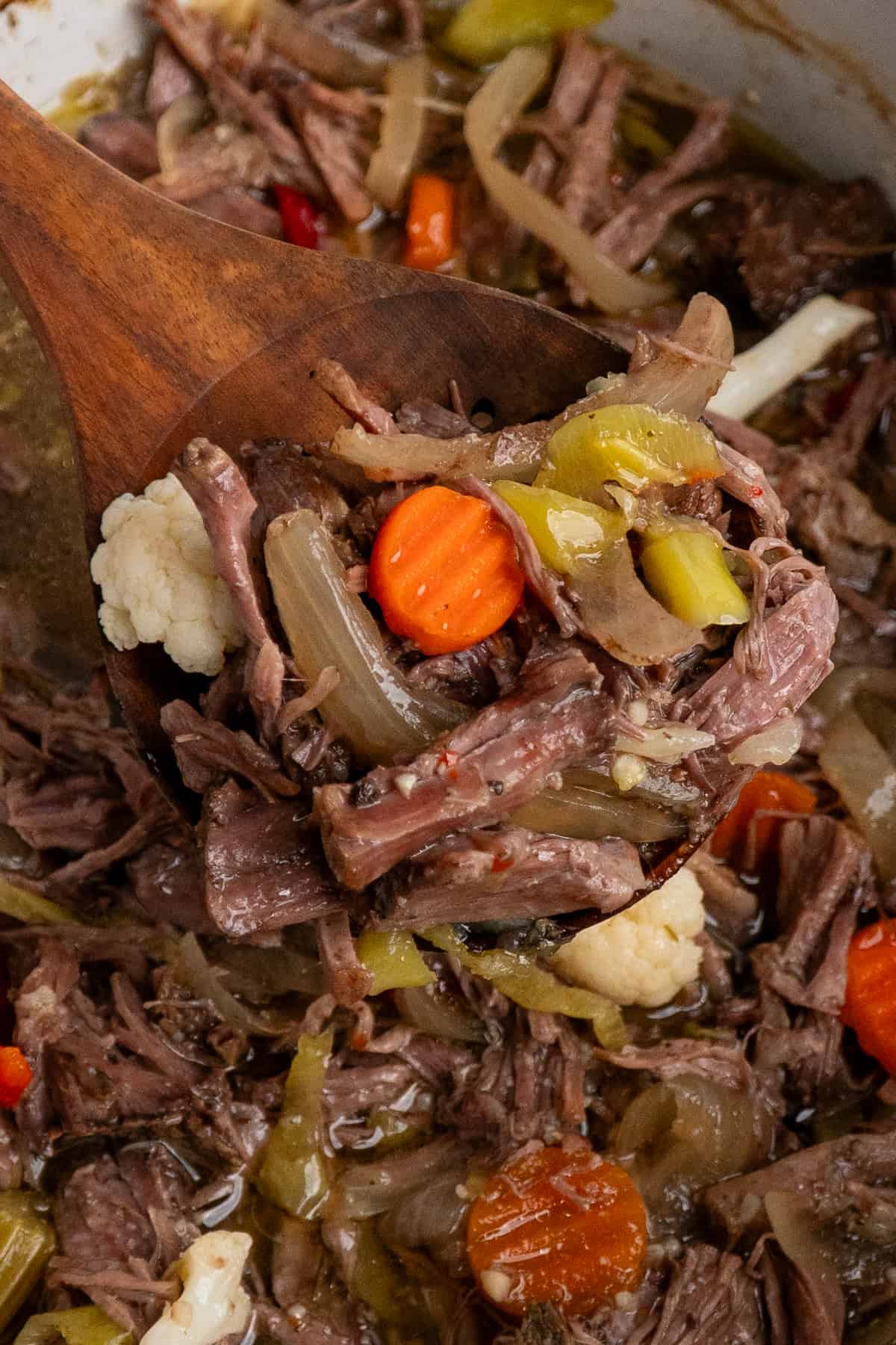 A wooden spoon holding Italian beef over a crock pot.