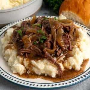 Close-up of French onion pot roast over a plate of mashed potatoes.