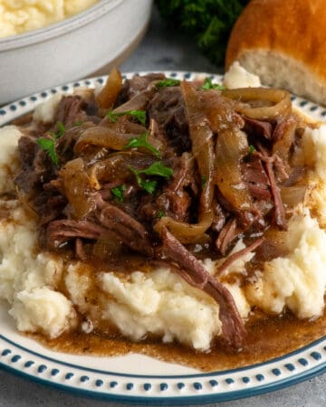 Close-up of French onion pot roast over a plate of mashed potatoes.
