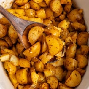 A wooden spoon holding a scoop of slow cooker roasted potatoes.