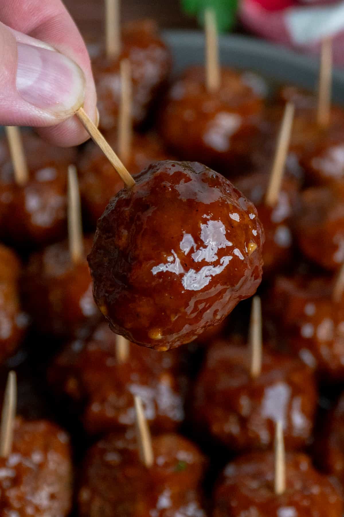 A hand holding a BBQ meatball on a toothpick.