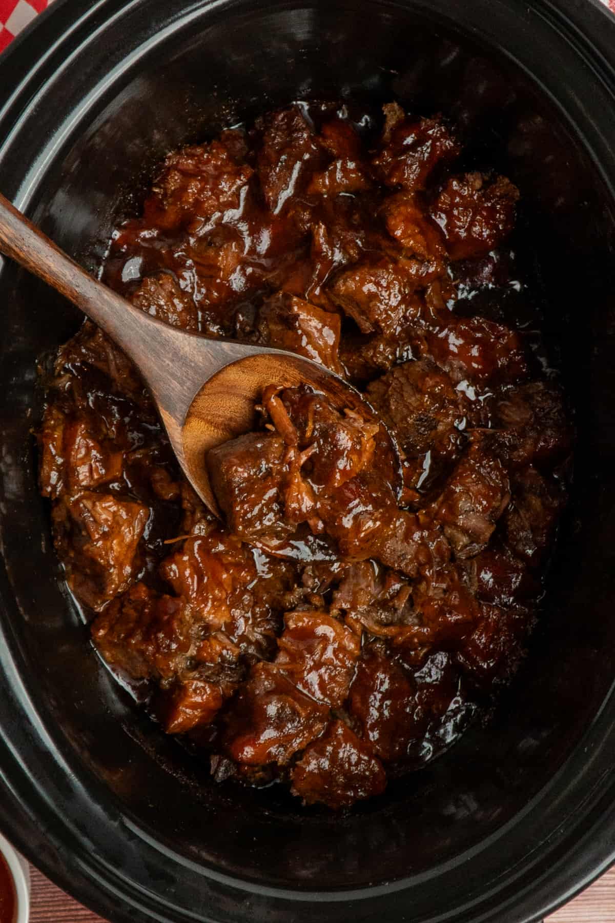 A wooden spoon holding burnt ends over a slow cooker.