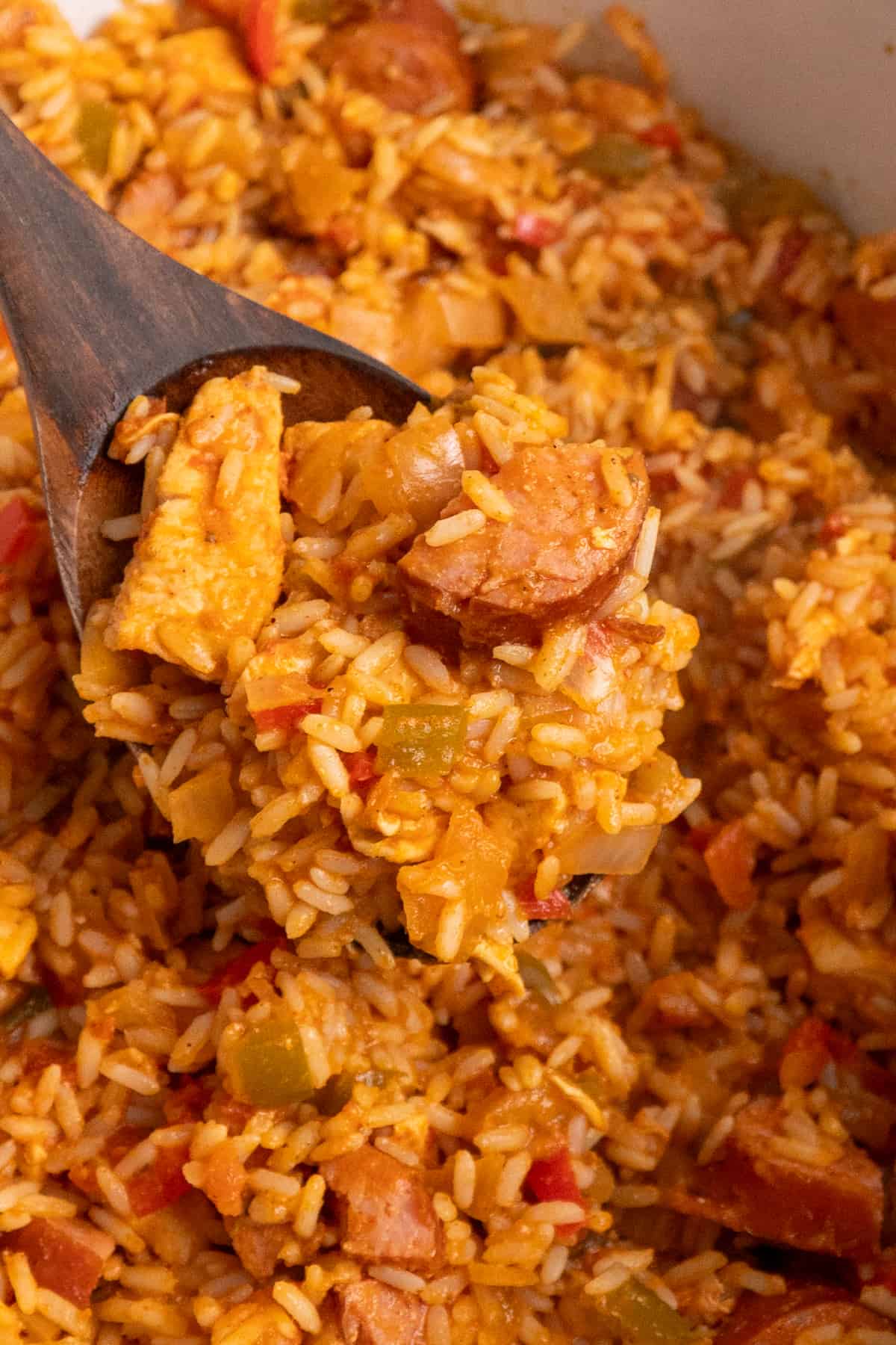 A wooden spoon holding jambalaya over a slow cooker.