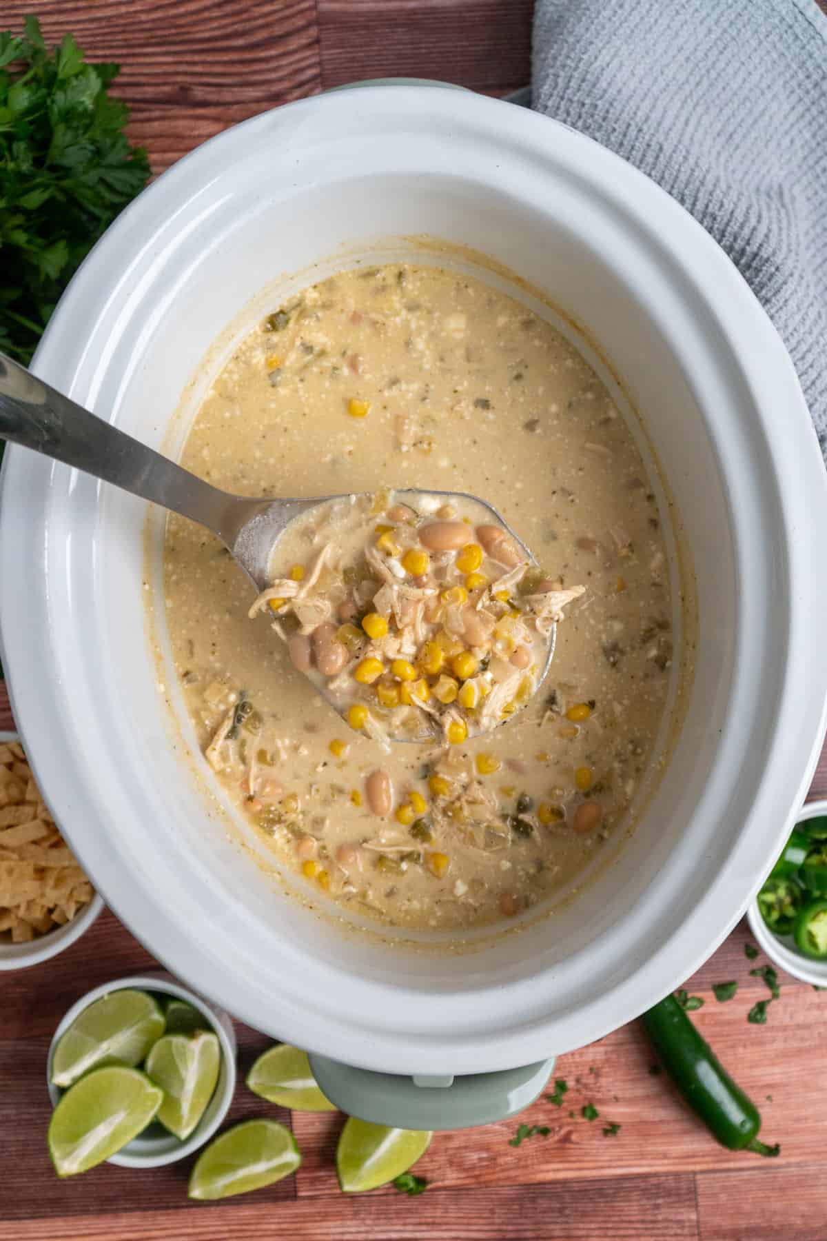 A ladle full of white chicken chili over a slow cooker.