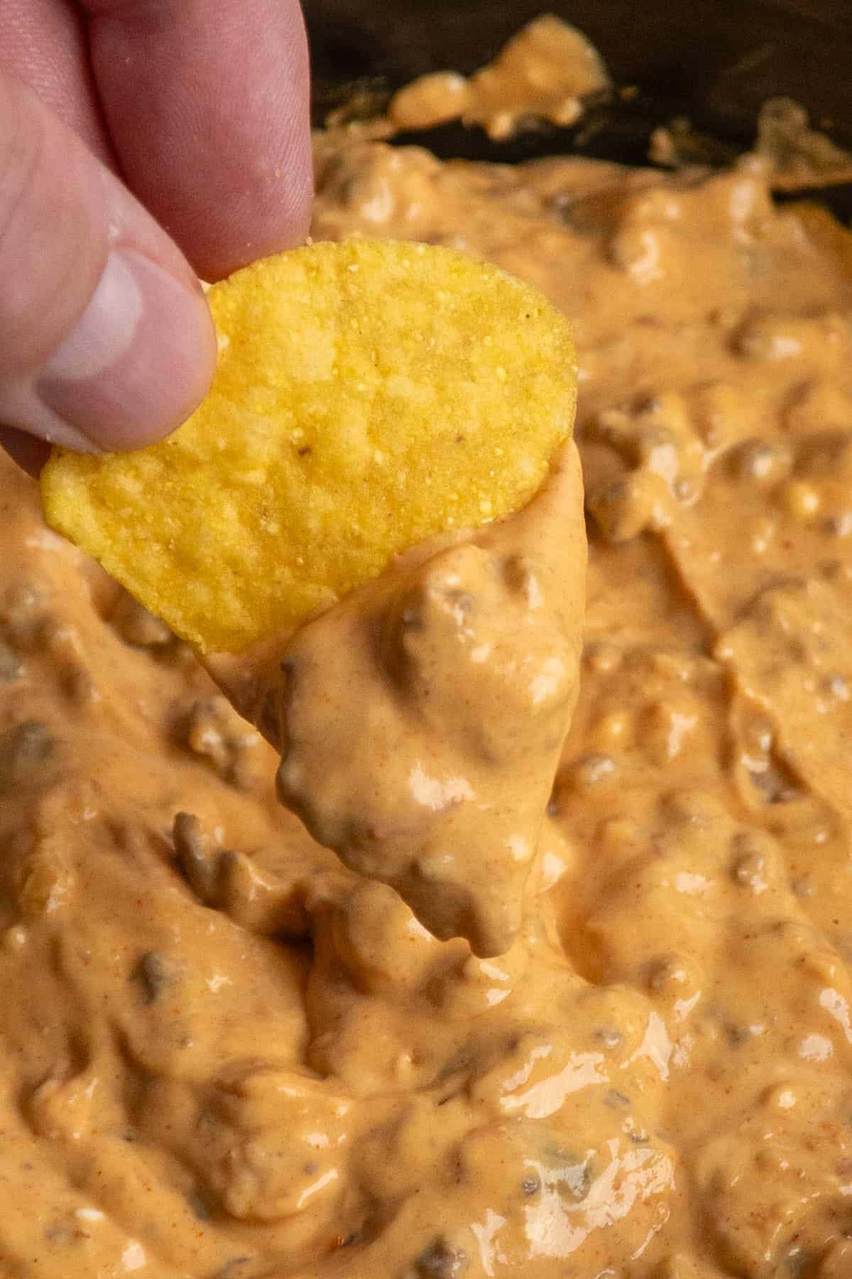 A hand holding a tortilla chip that has been dipped into taco dip.