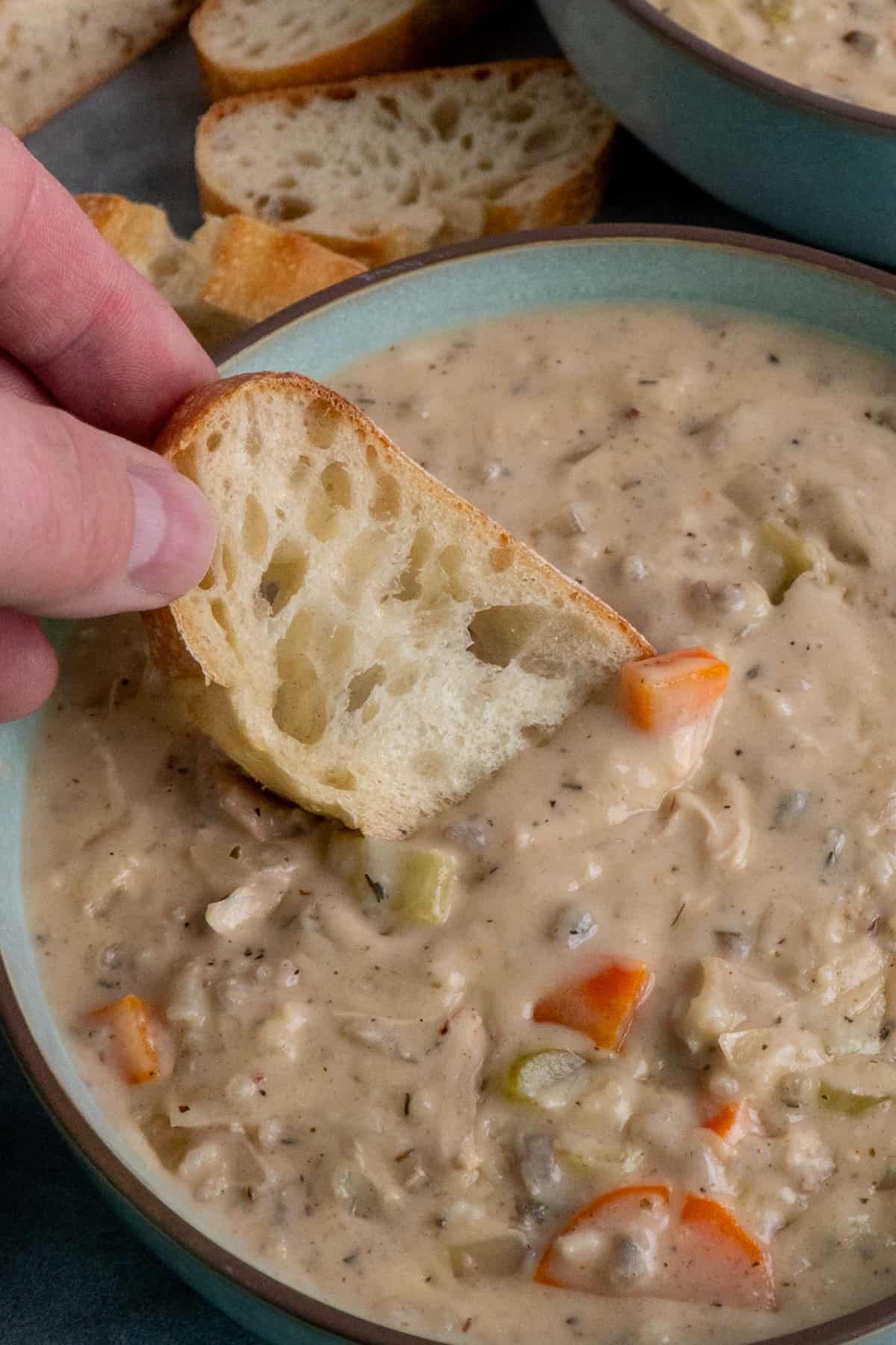 A hand dunking a piece of bread int chicken wild rice soup.