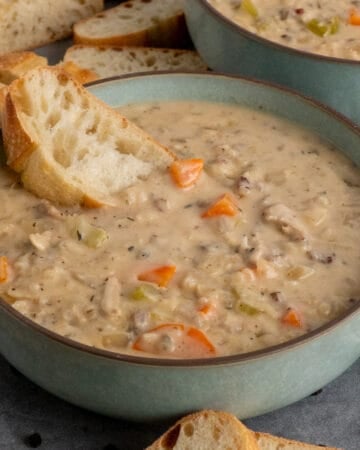 A piece of bread in a bowl of chicken wild rice soup.